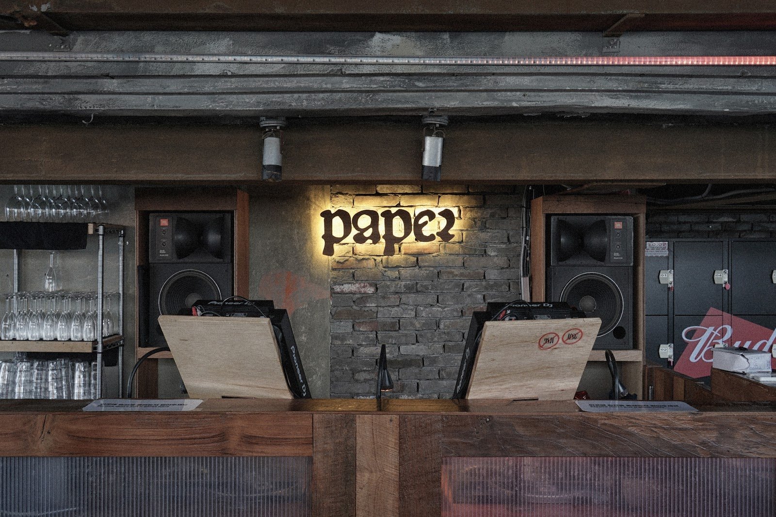 A frontal view of PAPER’s DJ booth, flanked by speakers beneath the physical venue sign.